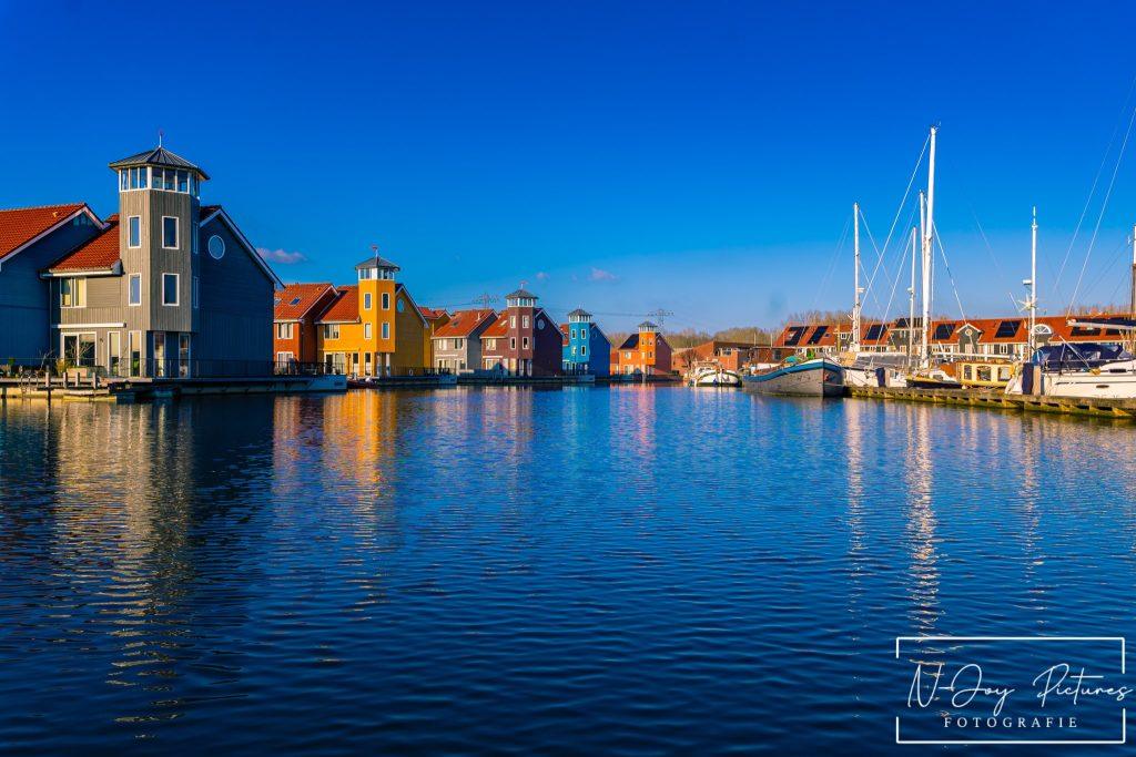 Levendige Plekken van Reitdiephaven Groningen Ontmaskerd! 3 Kleurrijke huisjes aan de Reitdiephaven in Groningen weerspiegelen in het kalme water, met een serene sfeer die perfect is voor stadsfotografie.